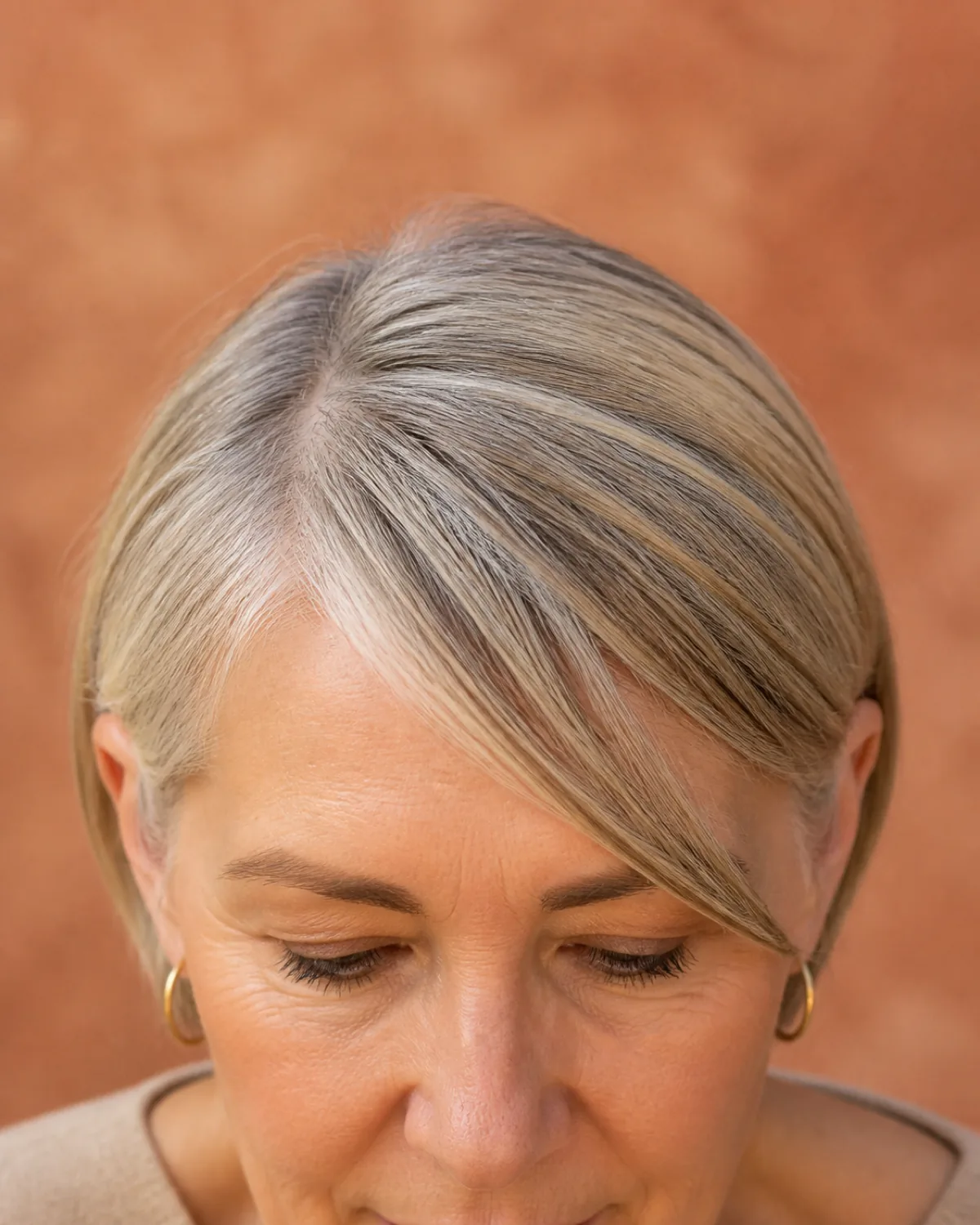 A close crop on the fringe and brow line of a woman with sandy-grey hair, a narrow side-swept fringe falling diagonally across the forehead with the longest piece reaching just past the outer brow corner