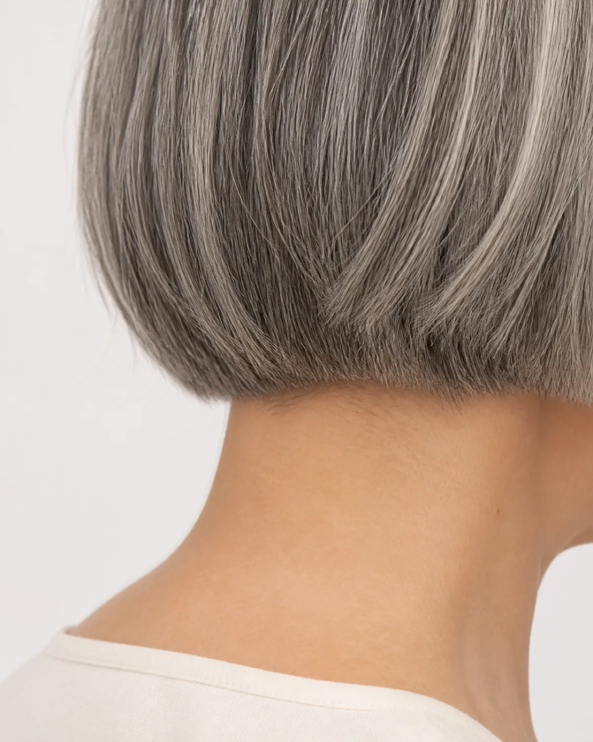 Close crop on the nape and hairline showing an ear-length grey bob with a clean nape line, the short length creating a wide horizontal reading