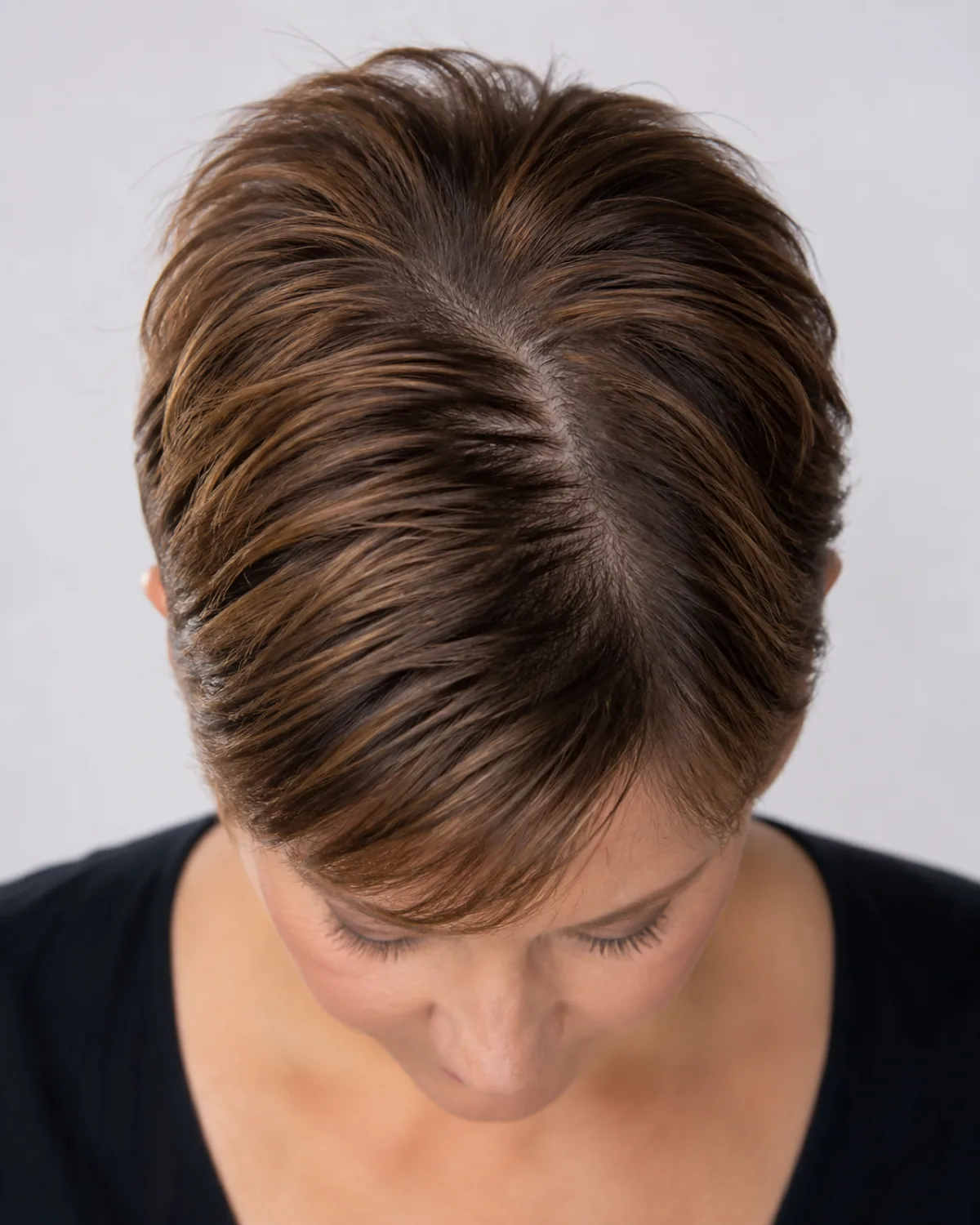 Top-down macro on the part line and root area showing a pixie growing out, the top hair approximately three to four inches long while the sides are still cropped short