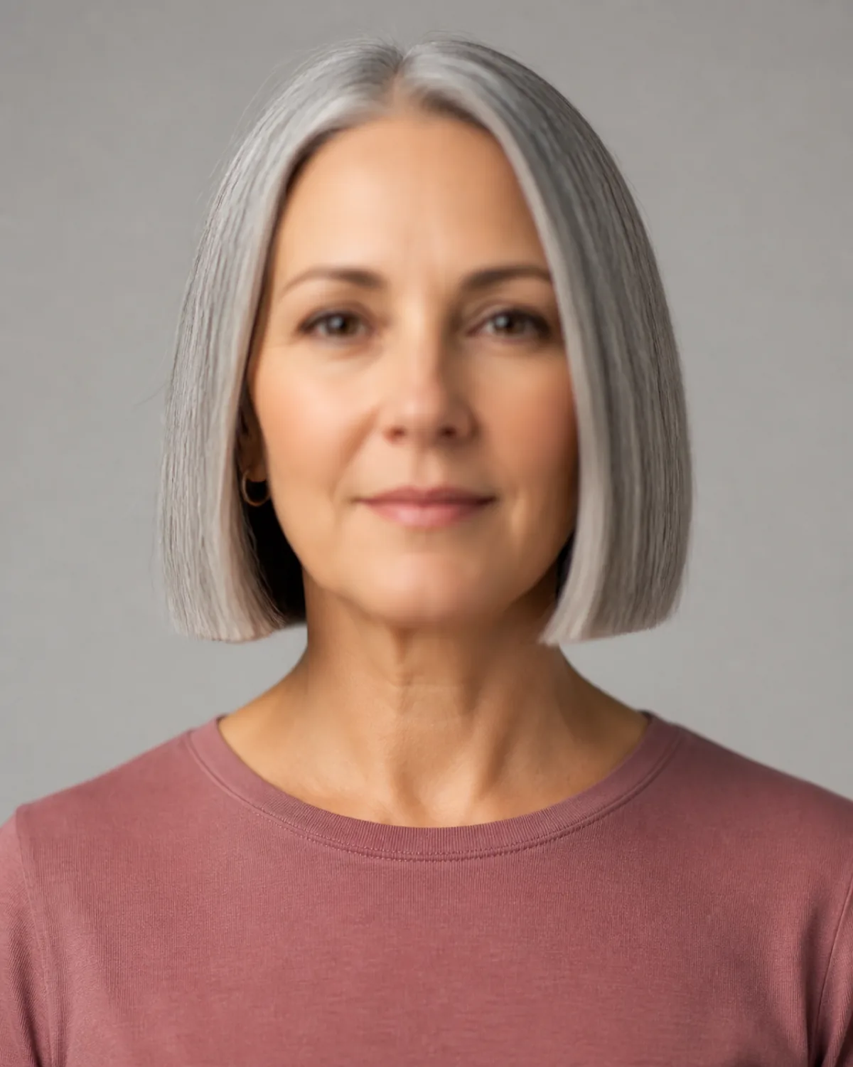 Front-facing woman over 50 with silver-gray chin-length blunt bob, even cut line at jaw, dusty rose top, soft focus on features