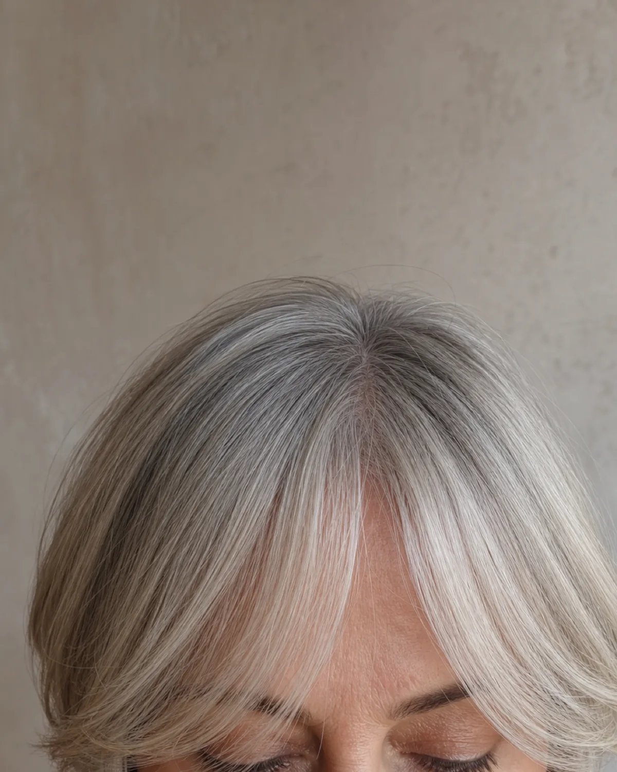 A close crop on the centre-parted fringe and brow line of a woman with fine silver-blonde hair, the shortest point of the curtain fringe sitting just above the brow with longer pieces sweeping outward
