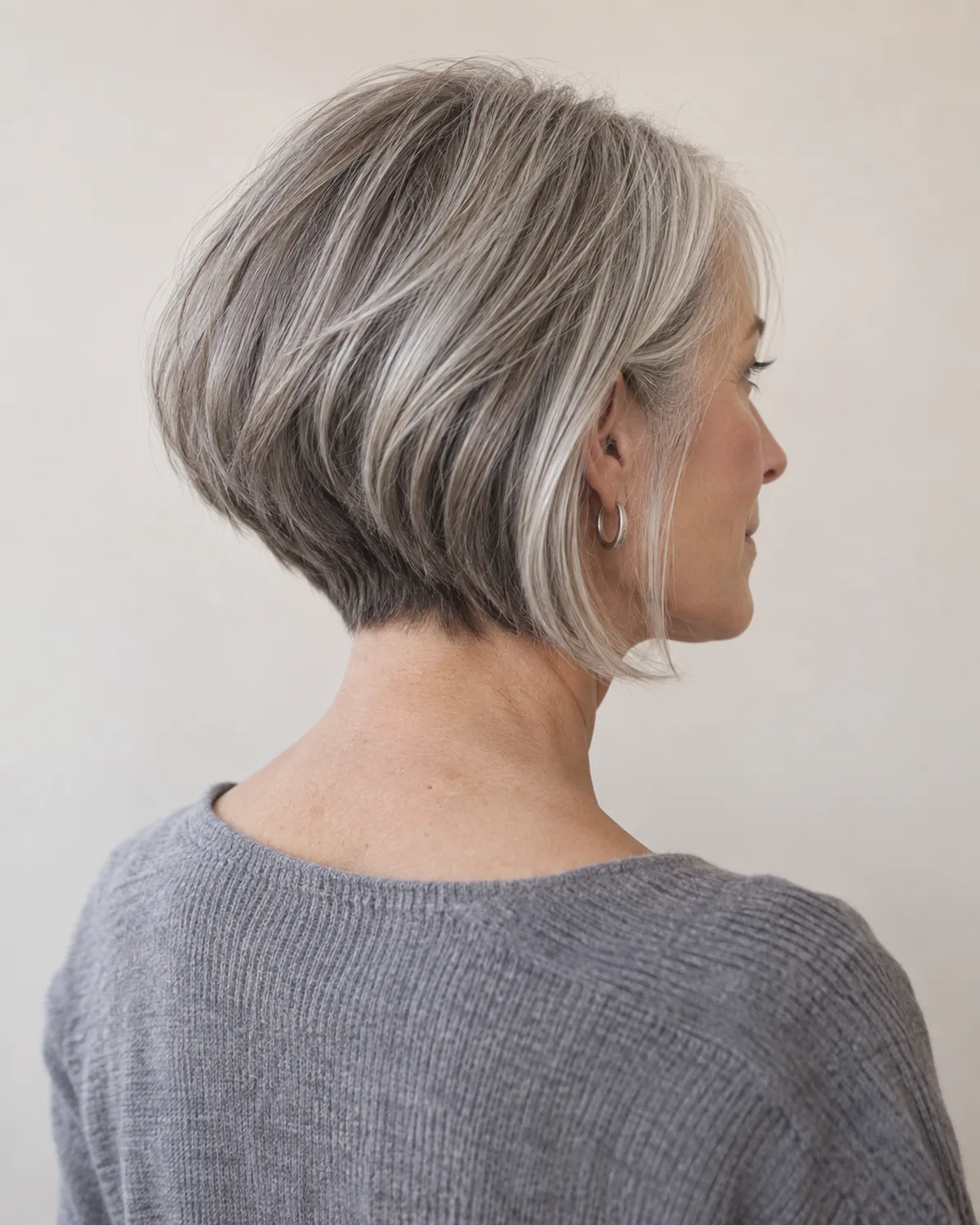 Back-three-quarter view of a mature woman with silver hair in a graduated bob showing stacked layers at the nape and the angled graduation from back to front