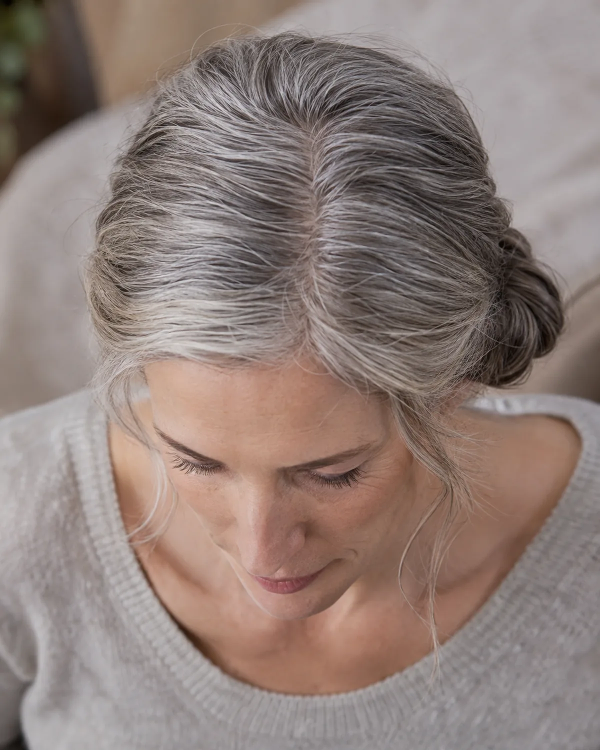 Top-down view of a mature woman with silver-grey hair in a low side bun, showing the part line and the off-centre placement of the bun at the nape