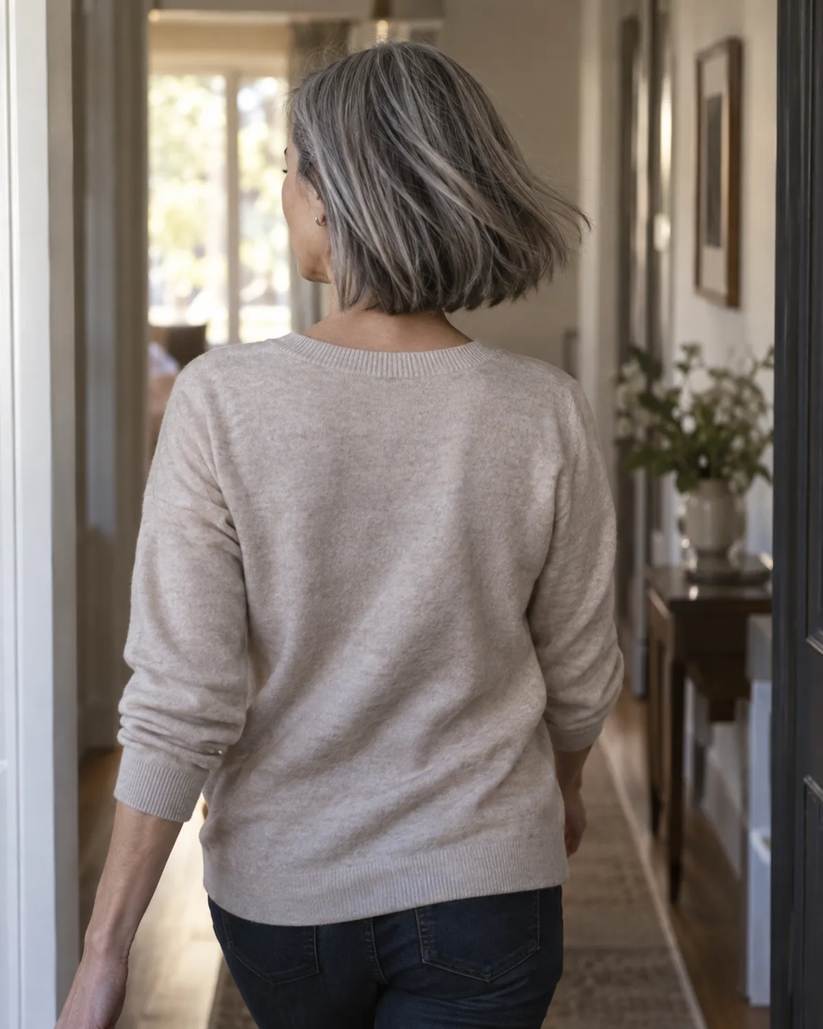 Back view of a mature woman walking away with silver-grey hair in a soft A-line bob, the shorter back and longer front visible in gentle motion