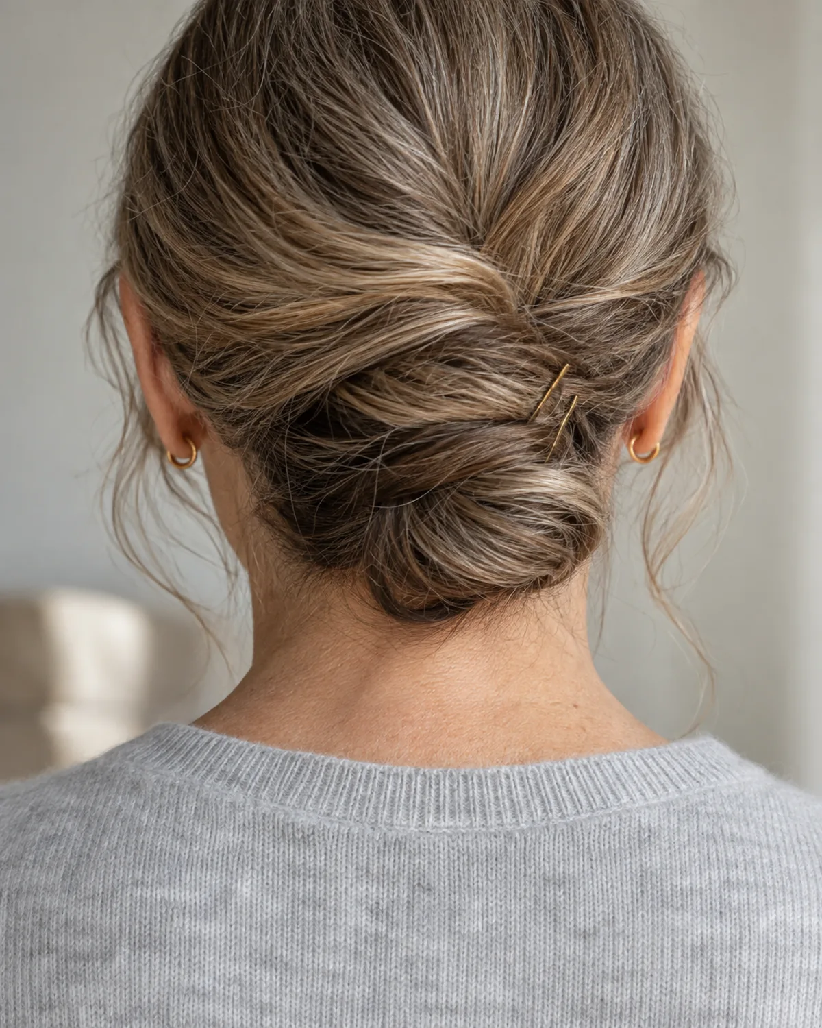 Close crop on the nape of a mature woman with long hair twisted into a low chignon held by plain pins, front pieces left out, pale-grey cashmere crewneck