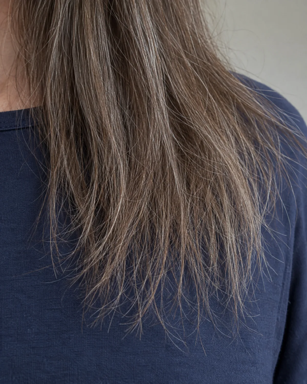 Close crop of fine hair ends at shoulder level showing thinning wispy strands separating with uneven perimeter, navy cotton top, flat natural light