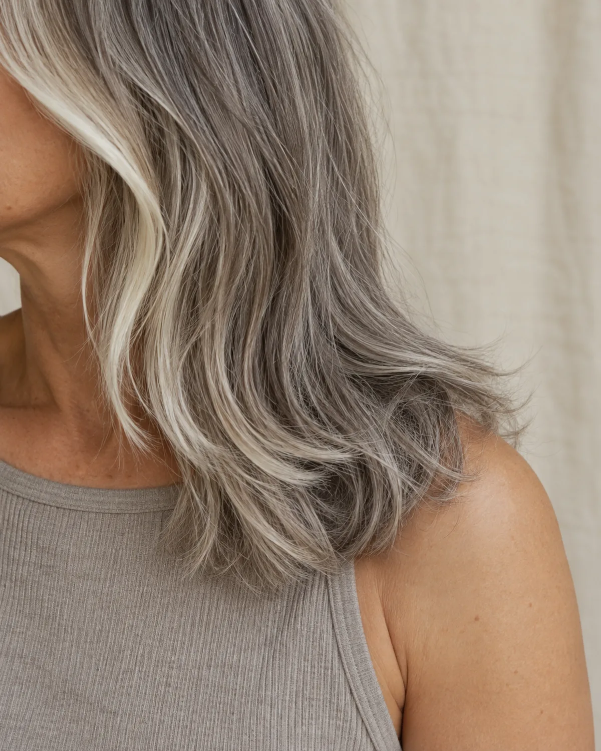 Close crop from mid-shoulder to tips of silver medium-length hair with lighter face-framing pieces at the front, warm cream linen background
