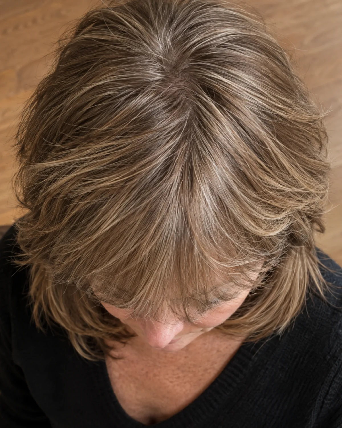 Top-down view of a woman over 50 with light brown feathered bangs blending into layered collarbone-length hair