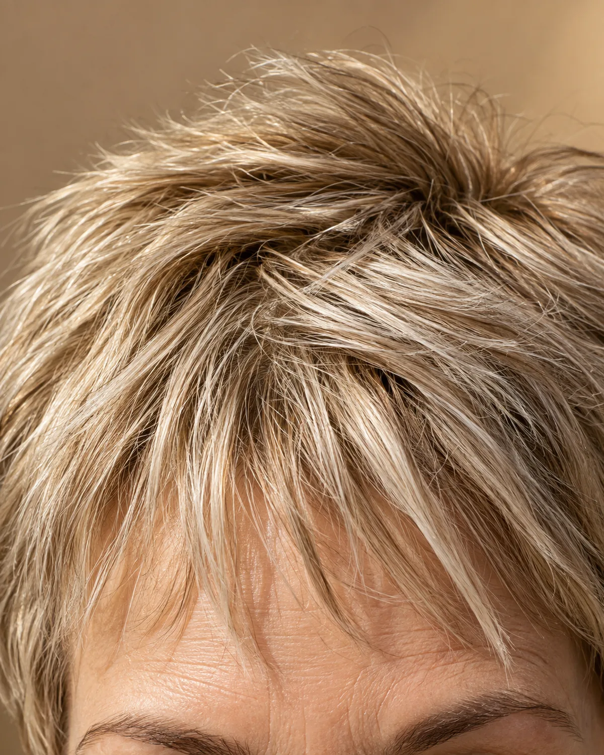 Close-up of choppy pixie bangs, sandy blonde with silver highlights, individual separated strands falling at different lengths