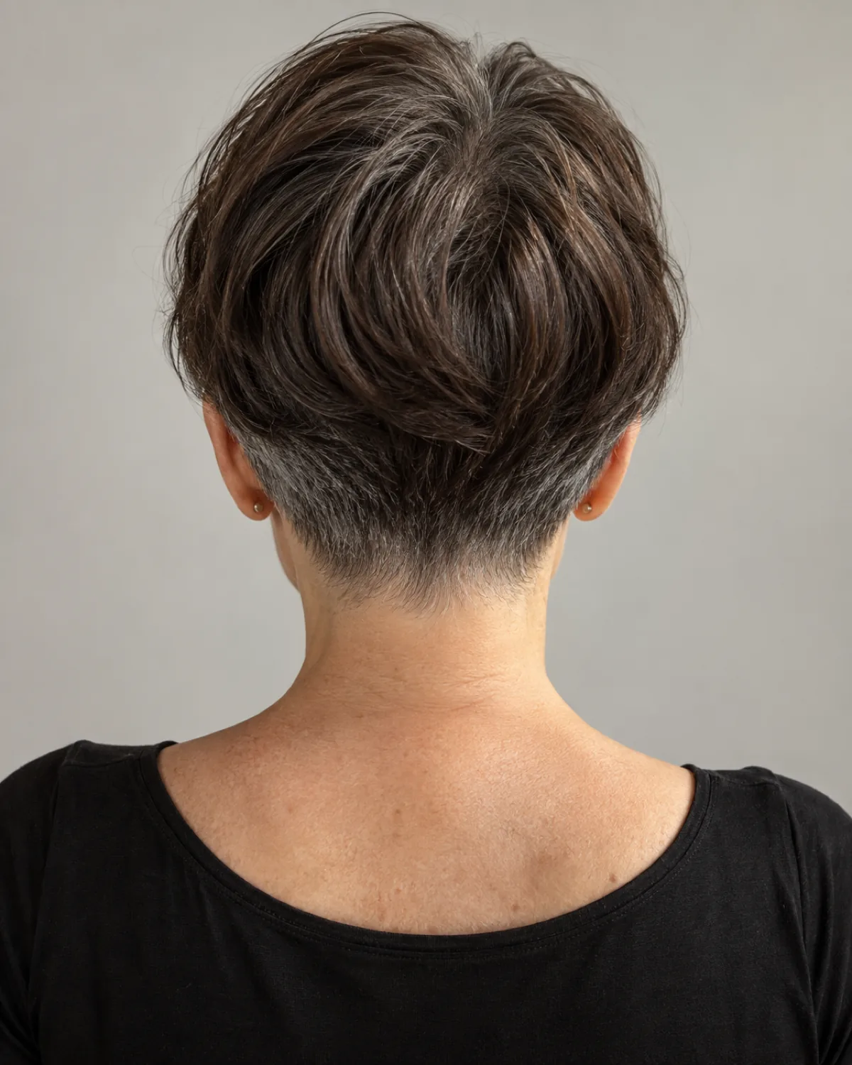 Back view of mature woman showing tapered nape with ear-length sides, dark brunette with grey, clean graduation visible