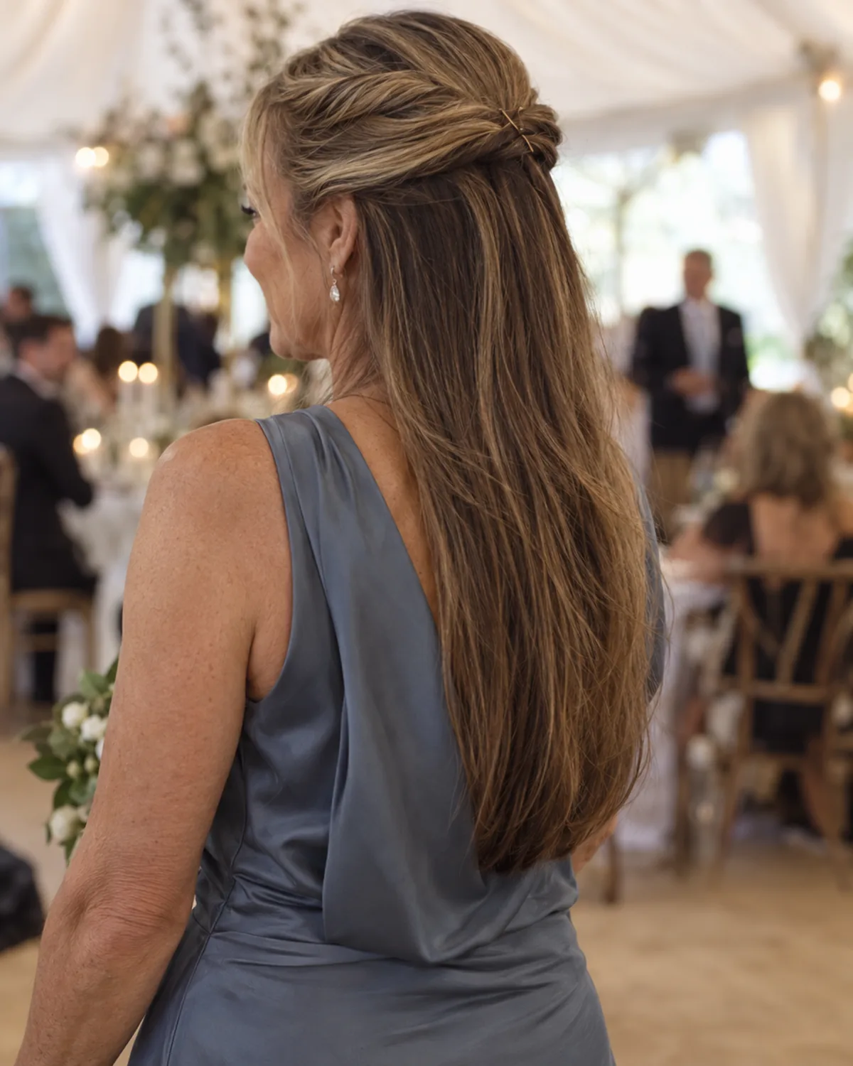 Back view of a woman over 50 in a slate-blue dress showing two rolled sections from each temple converging at the back of the crown with bobby pins